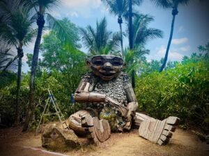 Large wooden troll sculpture among palm trees.