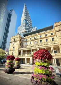 Historic building with modern skyscraper and flowers.