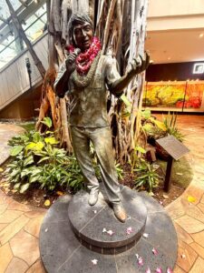Statue adorned with leis, microphone in hand.