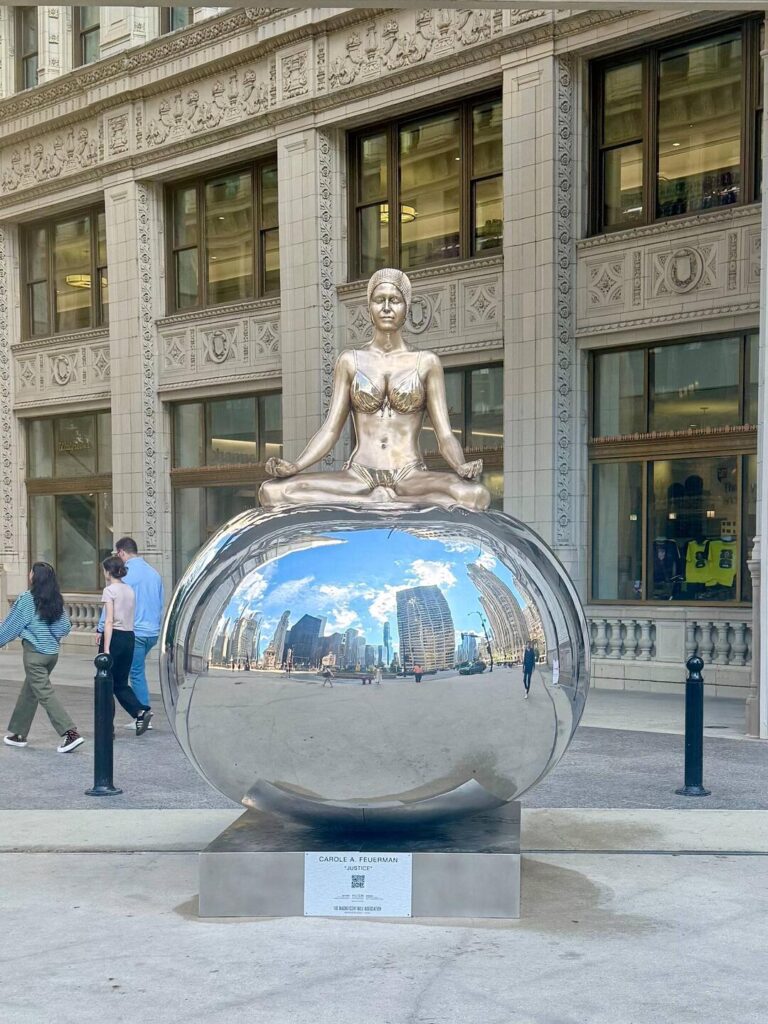 Reflective sculpture in front of ornate building.