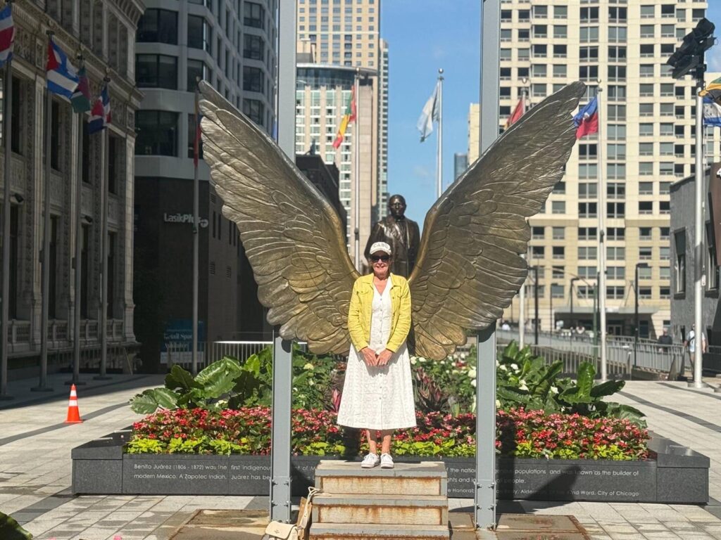Woman posing with winged sculpture in urban setting.