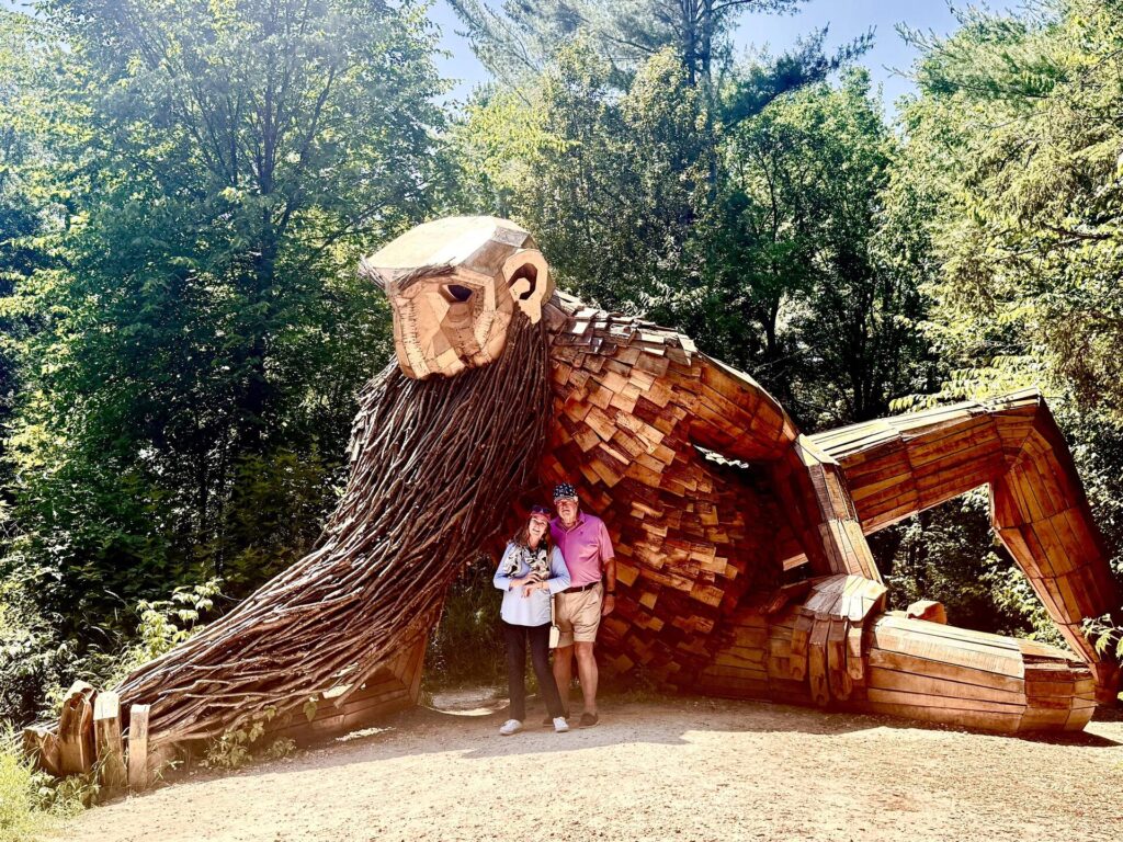 Couple with giant wood sculpture in forest.