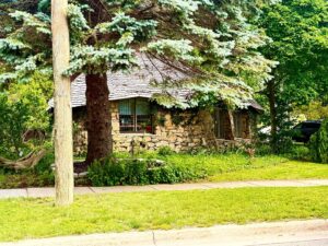 Stone cottage surrounded by lush greenery and trees.