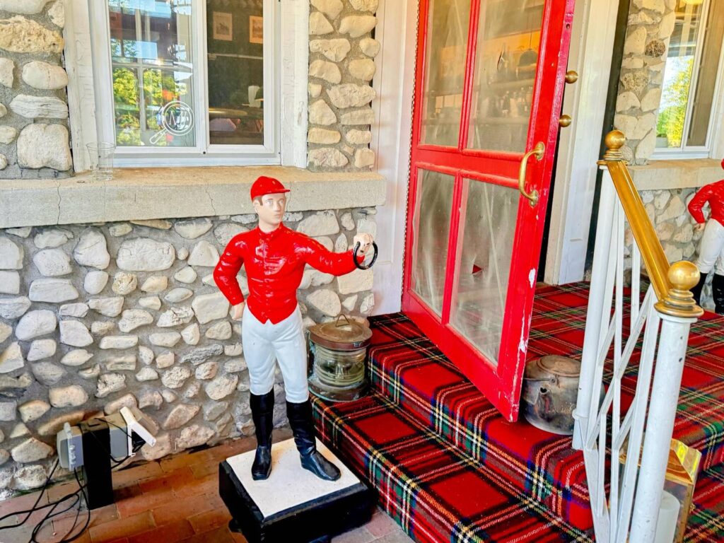 Red-jacketed jockey statue by stone wall and red door.