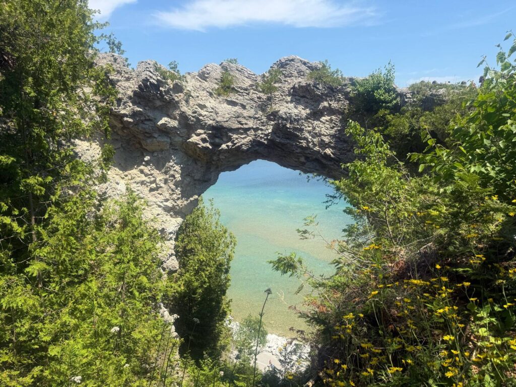 Natural arch over turquoise water with greenery.