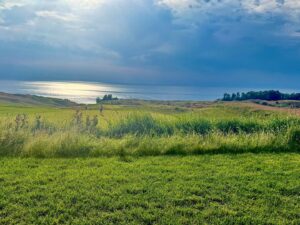 Sunlit golf course by the sea under cloudy sky.