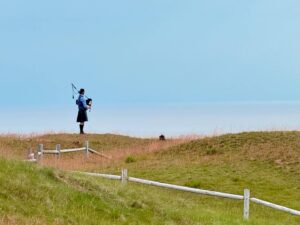 Bagpiper in traditional kilt plays on grassy hill.
