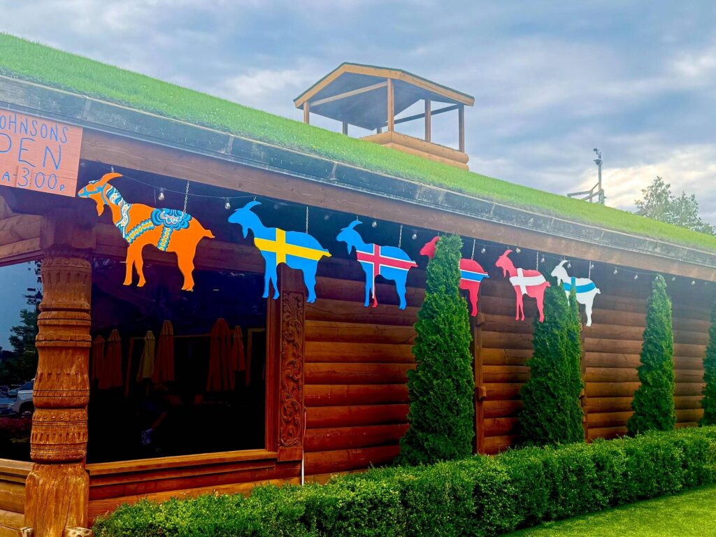Colorful goat flags on log cabin with grass roof.
