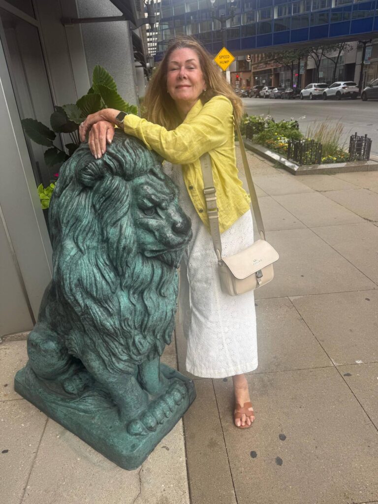 Woman hugging a lion statue on sidewalk.
