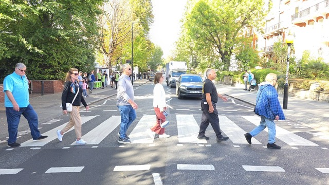 People crossing striped pedestrian crosswalk on sunny day.