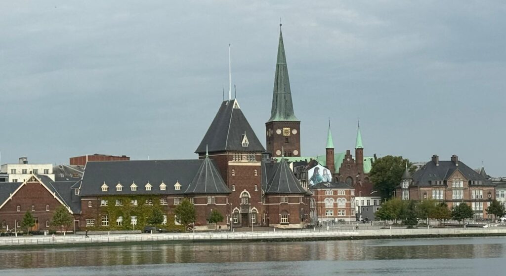 Historic building by waterfront with spires and trees.