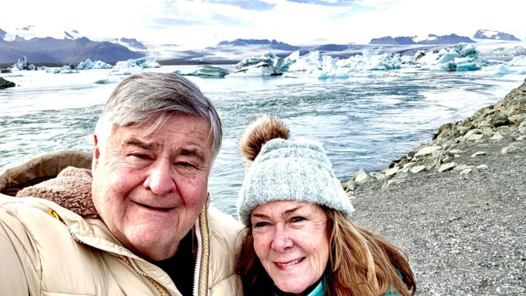 Couple smiling near icy landscape and river.