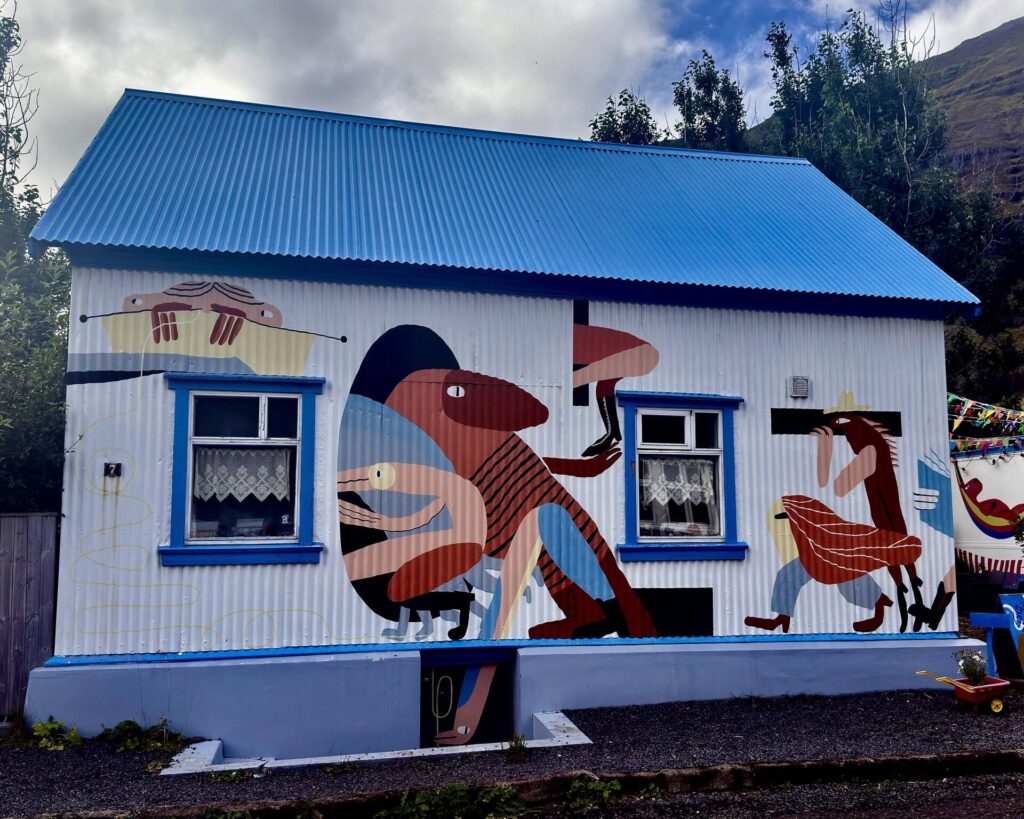 Colorful mural on a small house with blue roof.