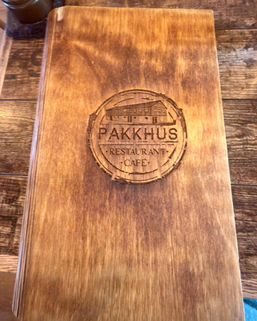 Wooden menu cover with engraved Pakkhus logo.