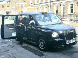 Smiling man beside open black taxi on street.