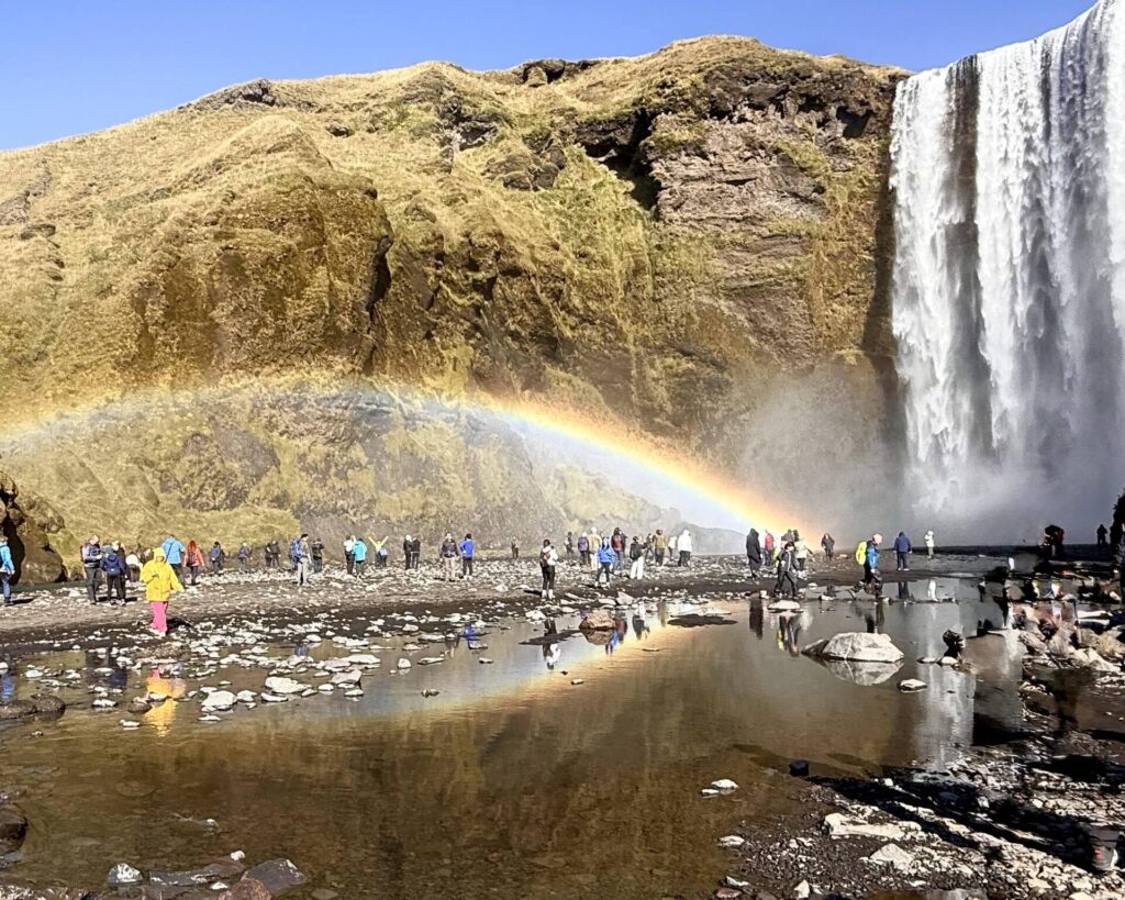 Tourists admire rainbow at waterfall base.
