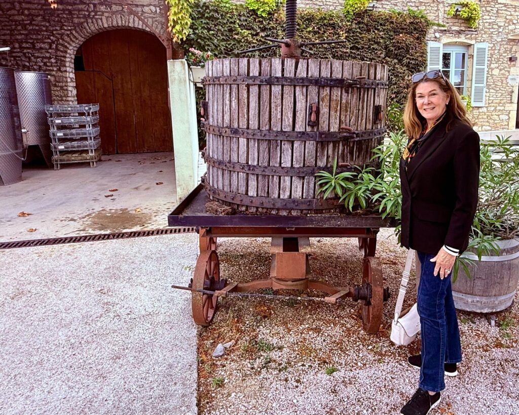 Woman standing by vintage wine press in courtyard.