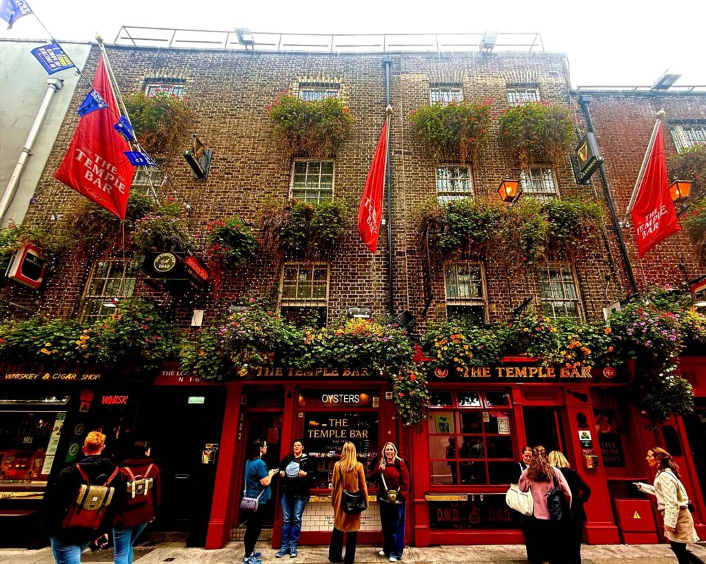 Historic pub with vibrant floral façade and red flags.
