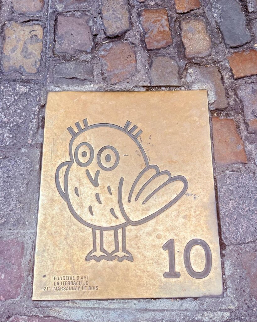 Bronze plaque with cartoon owl on cobblestones.